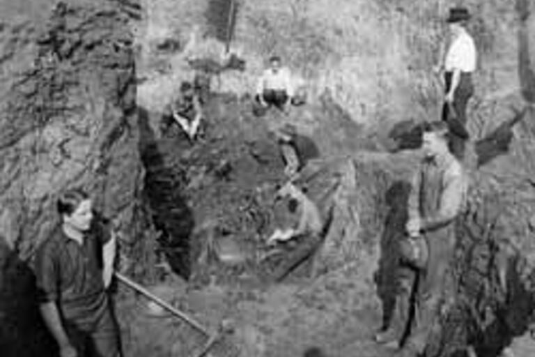 Young men stand around and inside a large excavation