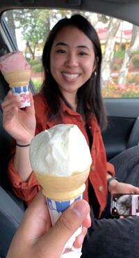 person holding ice cream cone with strawberry ice cream and smiling