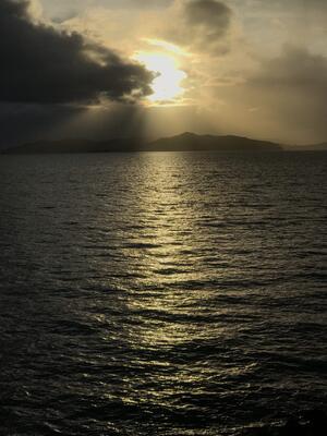 glistening ocean water with sun peaking out from behind the clouds 