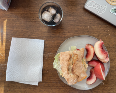 a sandwich on a plate with a side of sliced nectarines, a folded paper towel on the and a glass of soda with ice