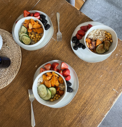 three meals bowls consisting of rice, chickpeas and cucumber as well as a side of berries placed on a wooden round table 