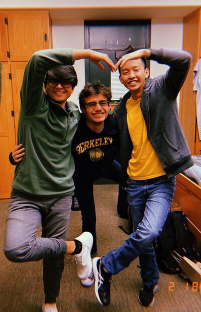 three students standing together in a dorm and smiling at the camera