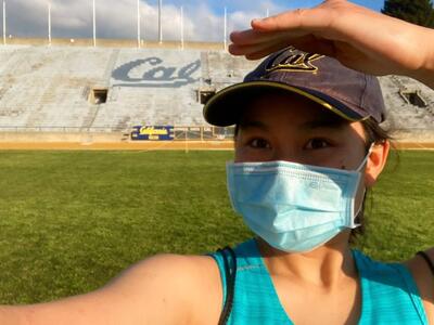student standing at the Cal stadium wearing a cal visor and mask on a sunny day